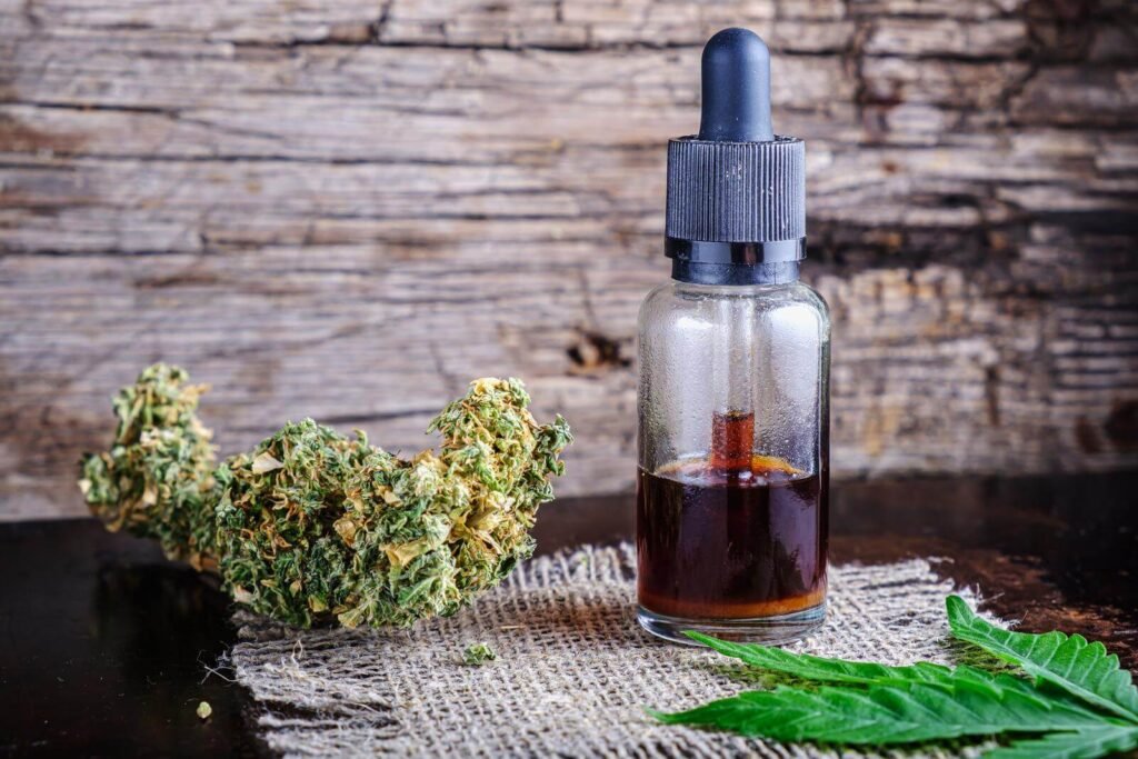 Brown medical cannabis resin extract in a dropper bottle, marijuana buds and hemp leaves.